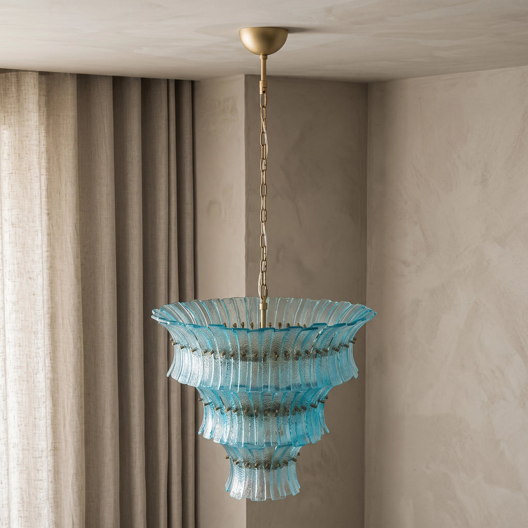 Aqua tiered glass chandelier suspended beside heavy draped curtains