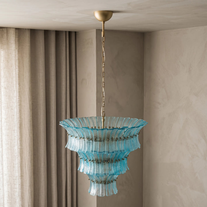 Aqua tiered glass chandelier suspended beside heavy draped curtains