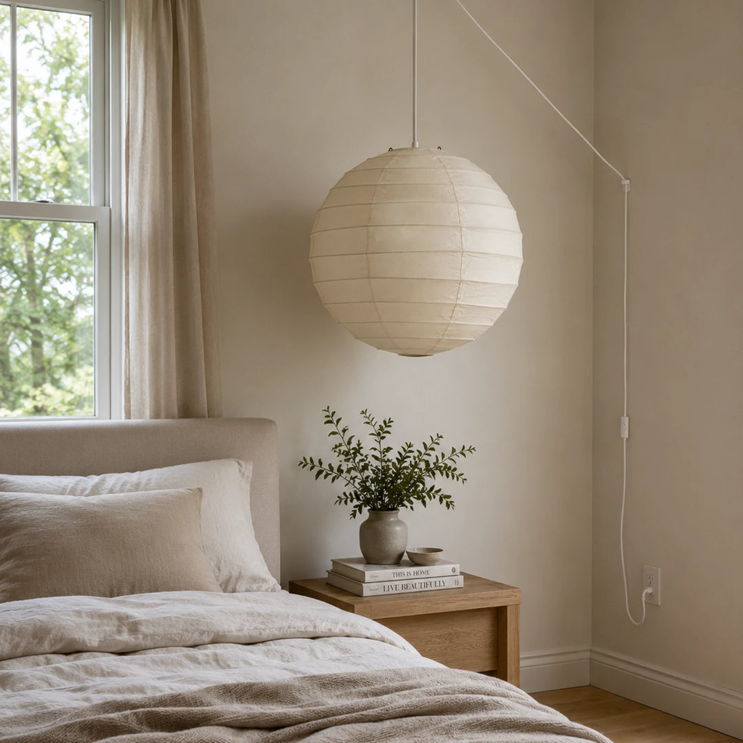 Paper pendant hanging beside a bed with soft linen bedding and greenery