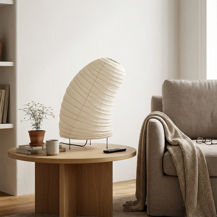 Curved paper table lamp glowing on a nightstand in a warm neutral bedroom