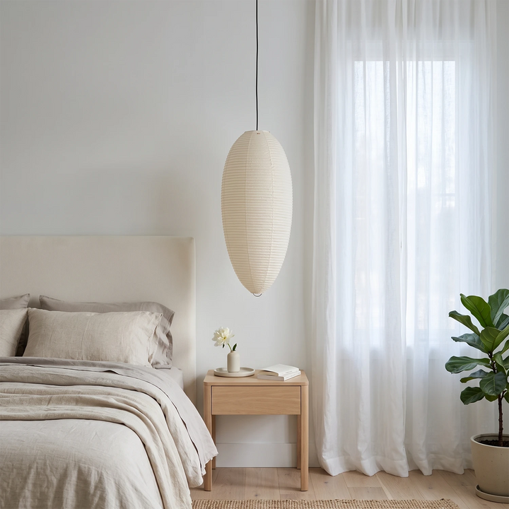 Oval paper pendant hanging beside a bed with soft linen bedding