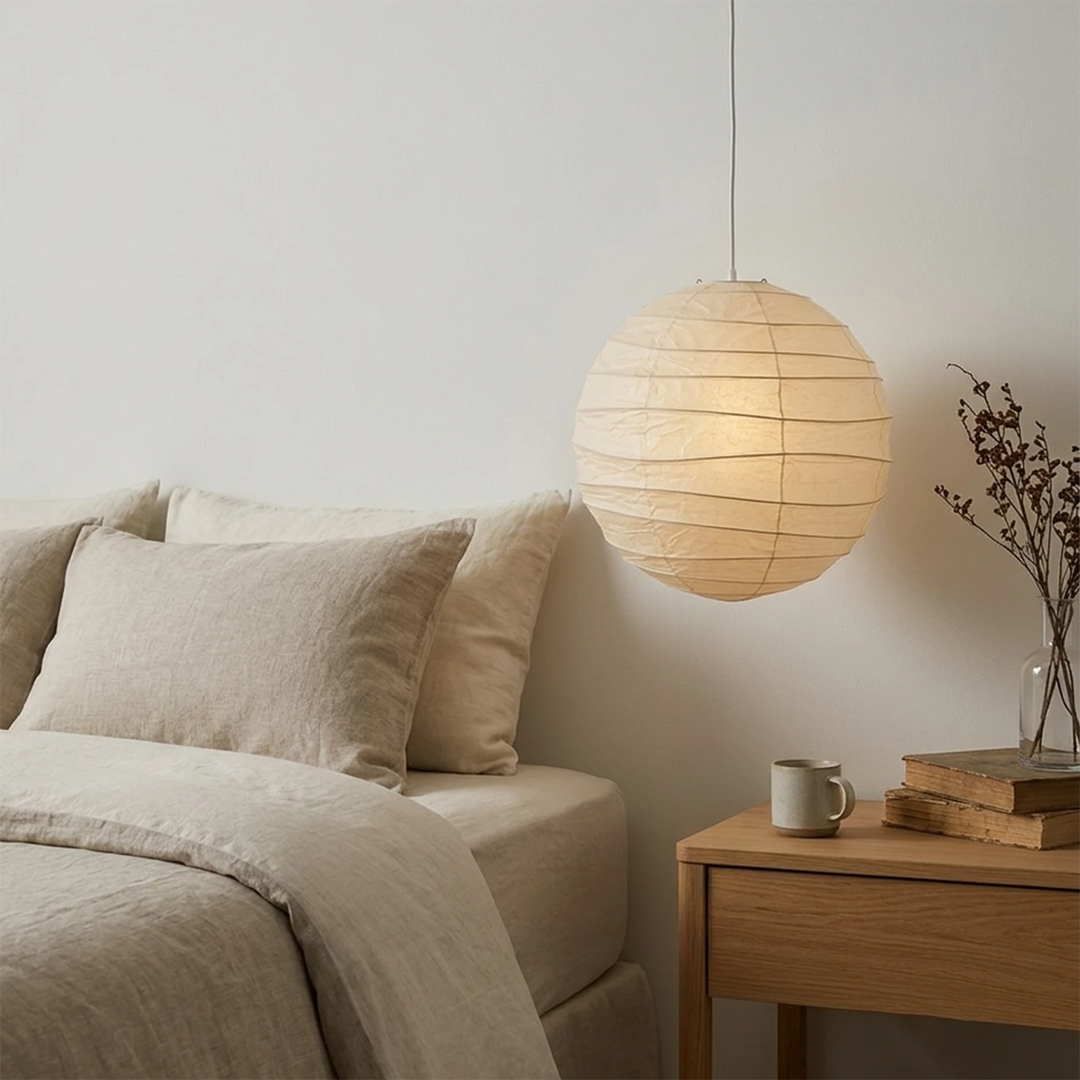 Paper pendant hanging beside a bed with soft linen bedding and a nightstand