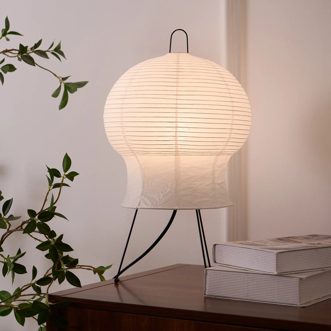 Bulb-shaped paper table lamp on a nightstand beside leafy branches