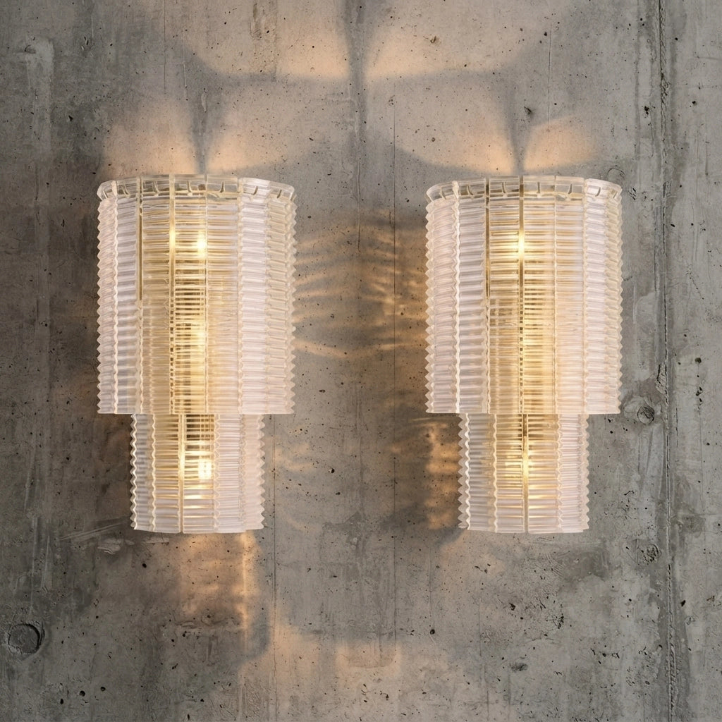 Pair of clear ribbed glass sconces casting soft light across a concrete wall