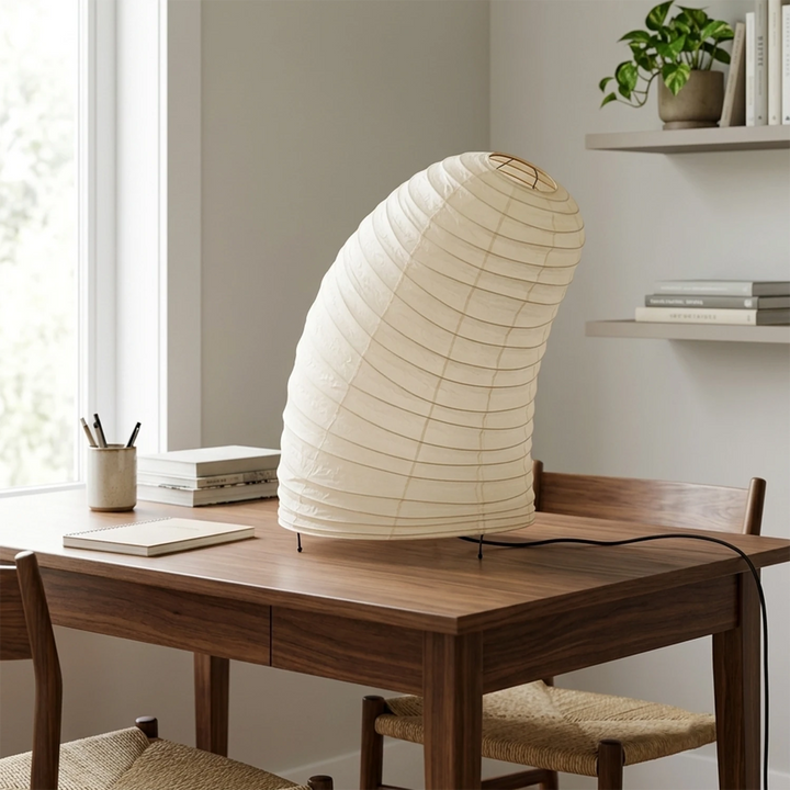 Curved paper table lamp on a wooden desk by a bright window