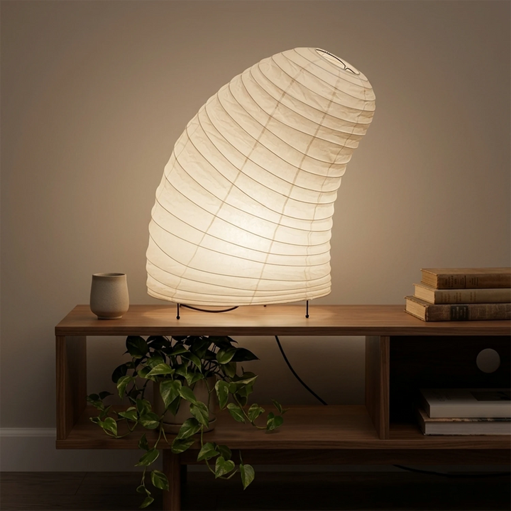 Shell-shaped paper lamp on a desk beside a tall fiddle-leaf plant
