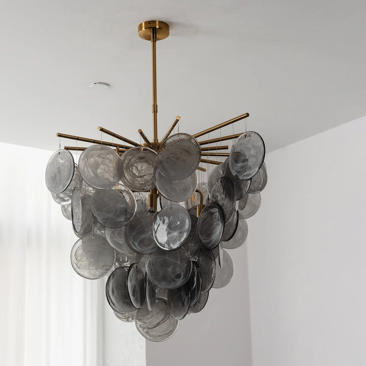 Glass disc chandelier shown at full drop against a white wall with its slim brass stem