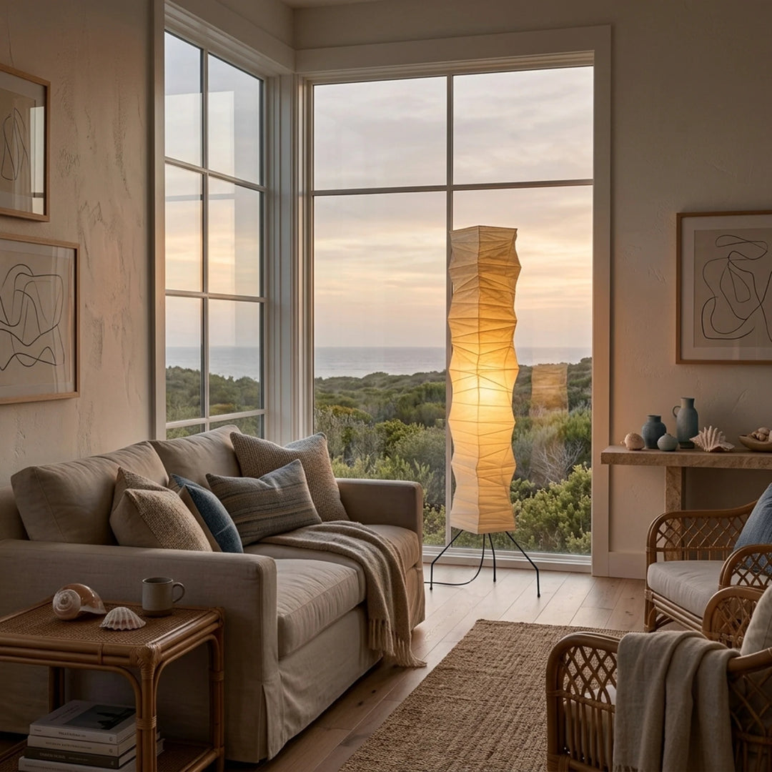 Paper floor lamp glowing beside a large window at golden-hour sunset
