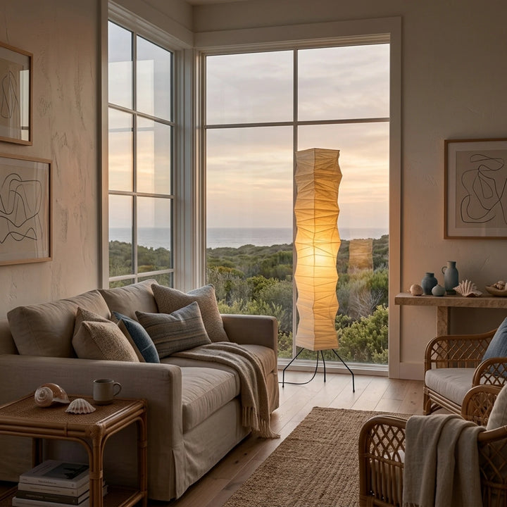 Paper floor lamp glowing beside a large window at golden-hour sunset