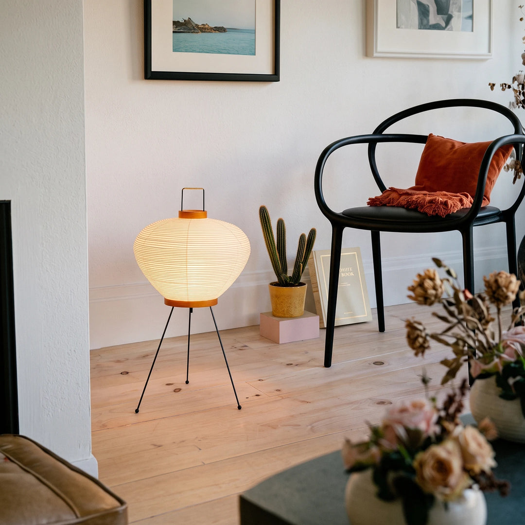 Handle lantern paper table lamp on a low bench beside a black bentwood chair and flowers