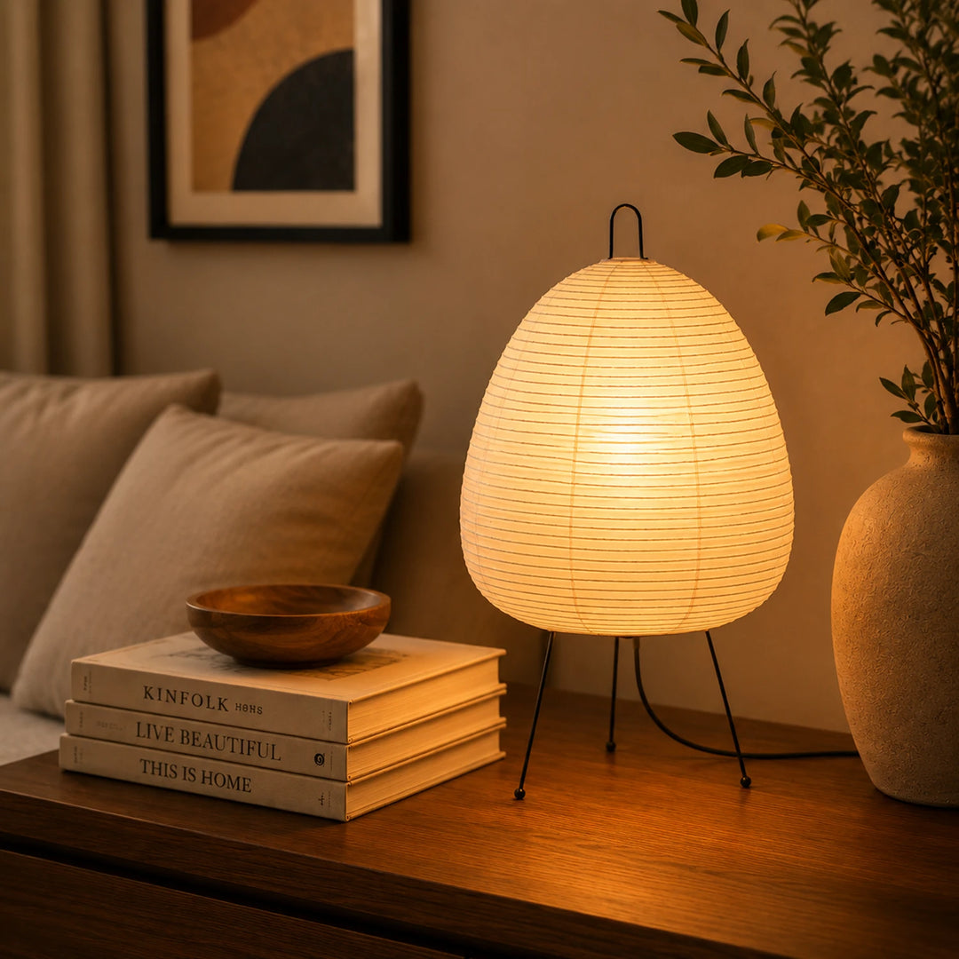 Paper table lamp casting warm light in a dark moody interior with stacked books