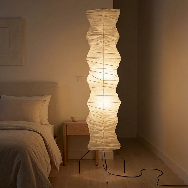 Glowing paper floor lamp beside a bed in a warm neutral bedroom corner