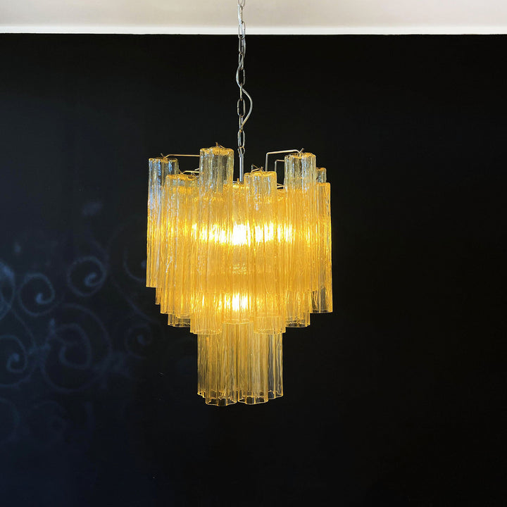 Murano Glass Tube Chandelier with amber gold glass lit with warm yellow light against a black wall
