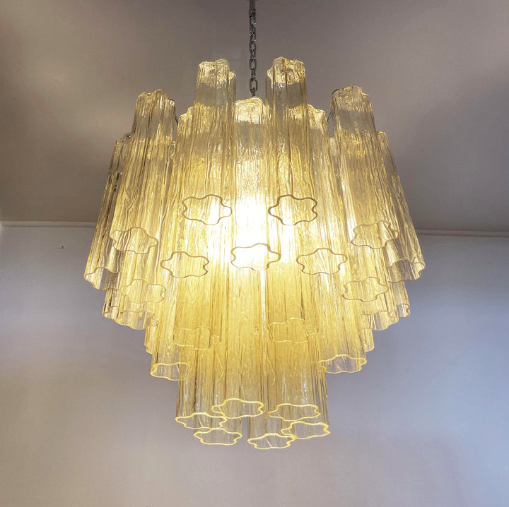 Lit Murano Star Tube Chandelier with amber glass tubes on a plain white wall