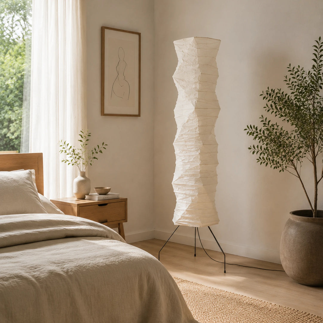 Paper floor lamp beside a bed and olive tree in a serene neutral bedroom