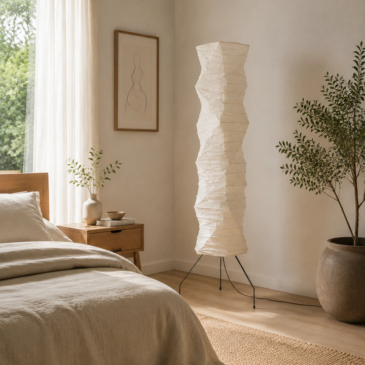 Paper floor lamp beside a bed and olive tree in a serene neutral bedroom