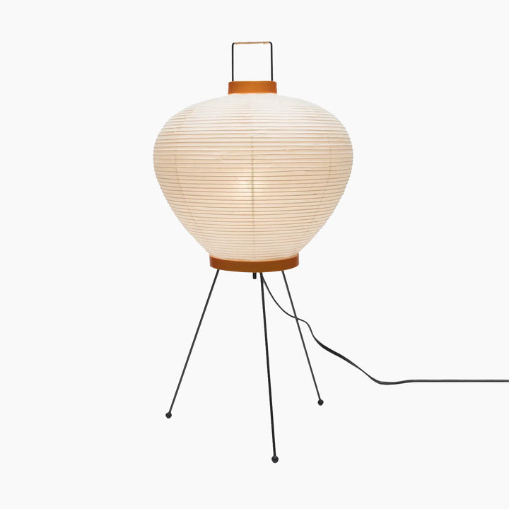 Oval paper table lamp photographed at an angle on a white background showing its wire tripod stand and trailing cord
