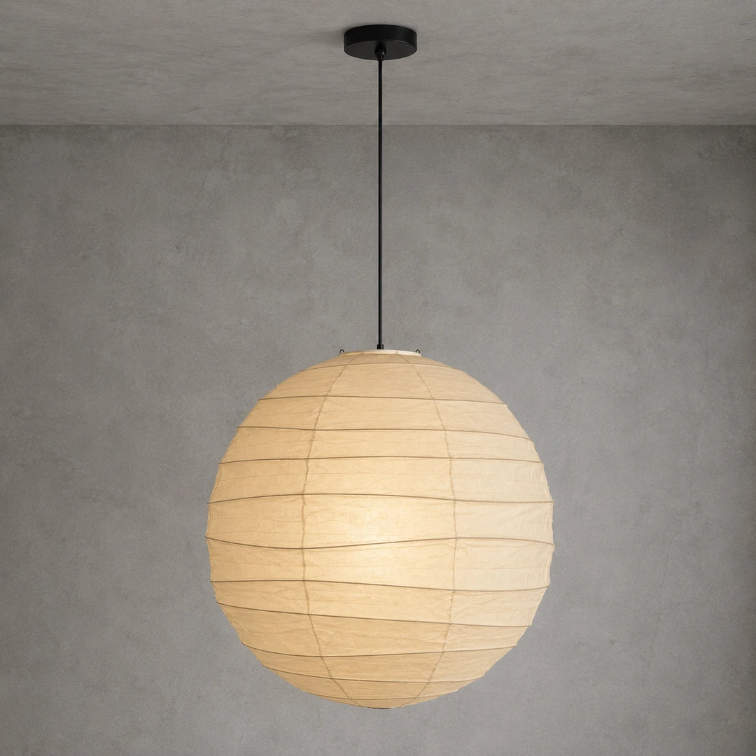 Paper globe pendant on a black cord hanging against a textured grey wall