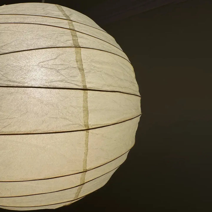 Paper globe pendant lit in a studio setting with soft shadow falloff