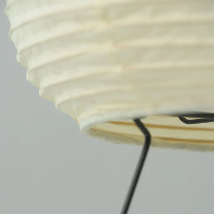 Close-up of the black metal tripod leg meeting the pleated paper shade at the base