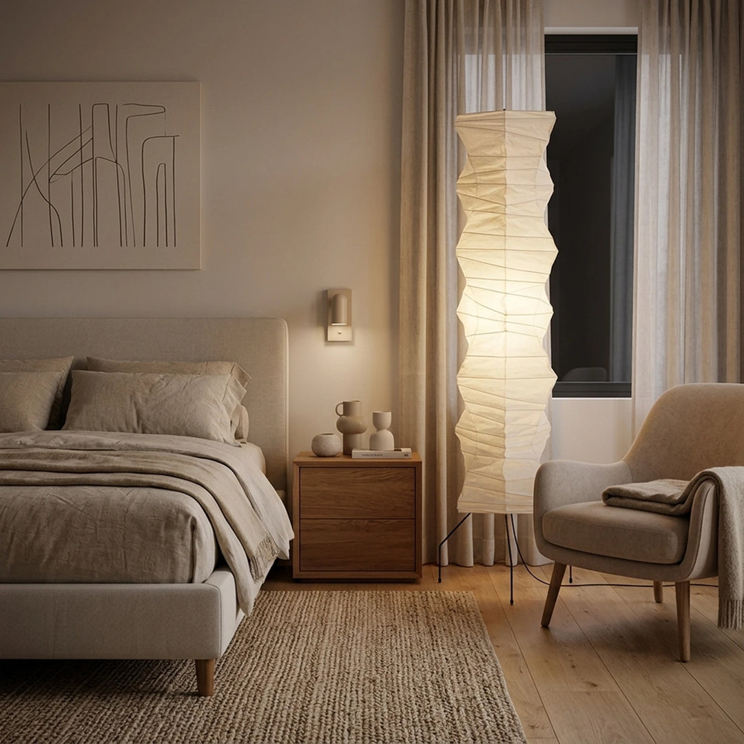 Paper floor lamp between a bed and armchair in a calm Scandinavian bedroom