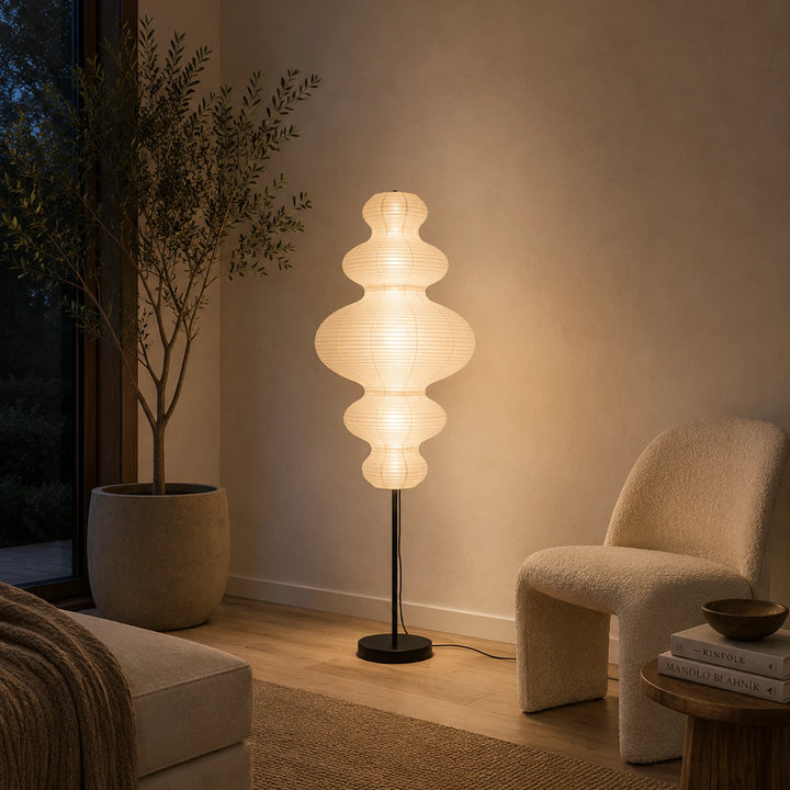 Sculptural paper floor lamp beside a bouclé armchair in a dusk-lit corner
