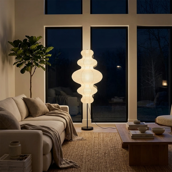 Sculptural paper floor lamp glowing beside dark evening windows in a lounge