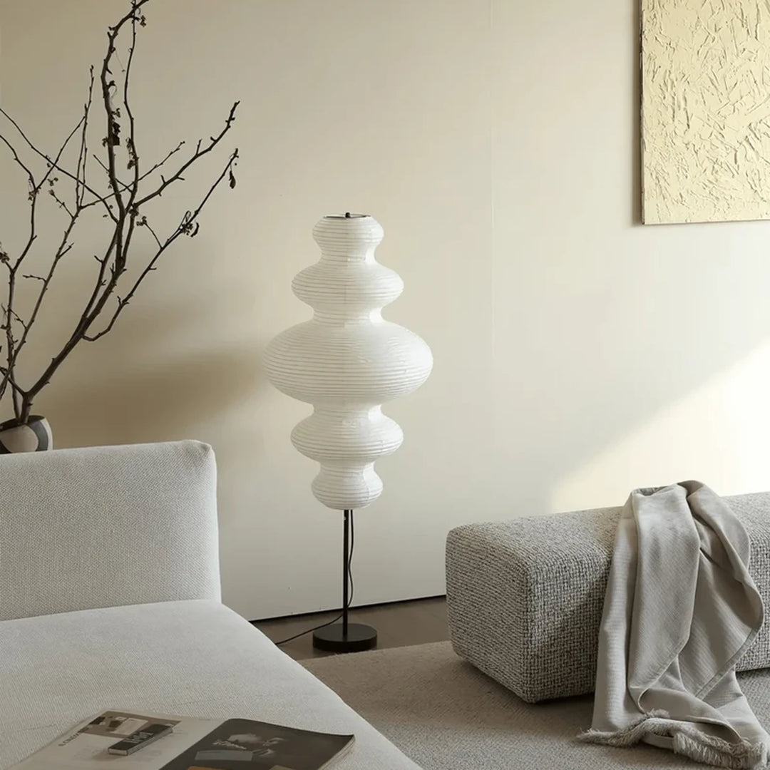 Sculptural paper floor lamp glowing in a minimal white living corner