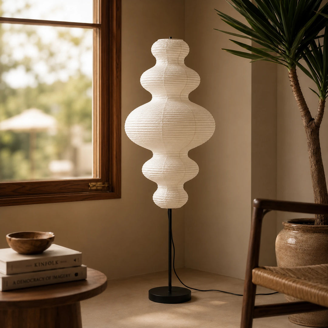 Sculptural paper floor lamp in a reading corner beside a tall plant