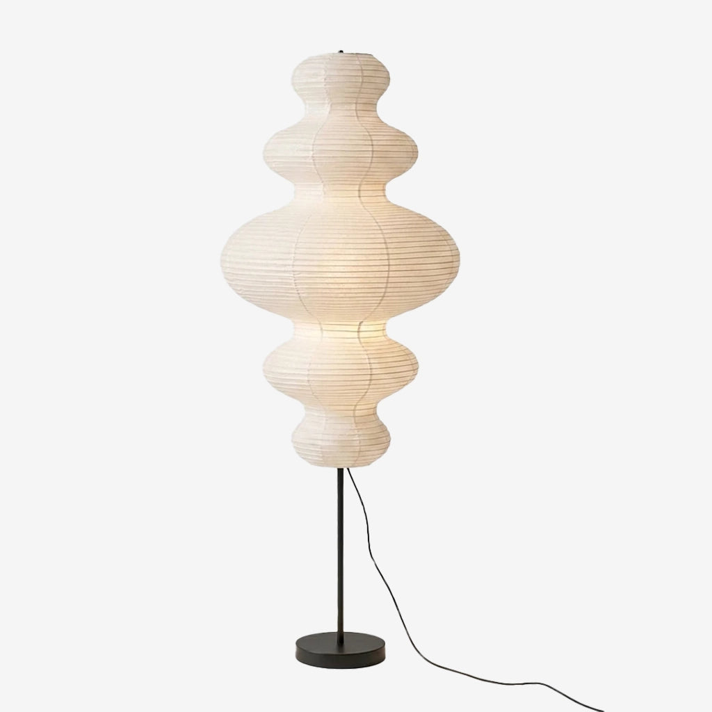 Sculptural paper floor lamp with stacked curved segments glowing softly above a slim black stem and round base, shown on a light gray background