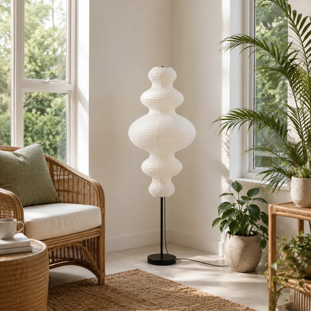 Sculptural paper floor lamp in a bright sunroom beside a rattan chair