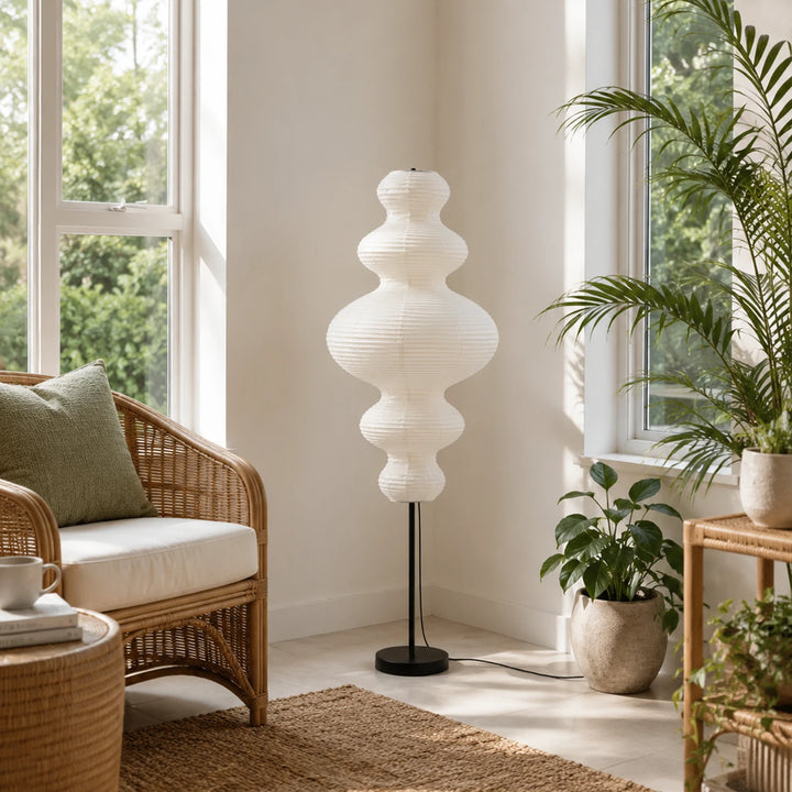Sculptural paper floor lamp in a bright sunroom beside a rattan chair