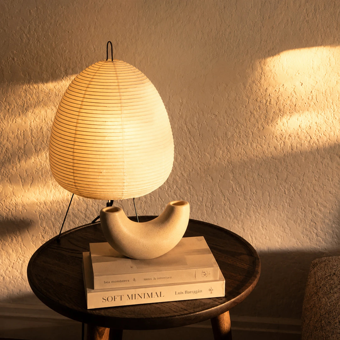 Sculptural paper lamp on a round black side table with stacked art books