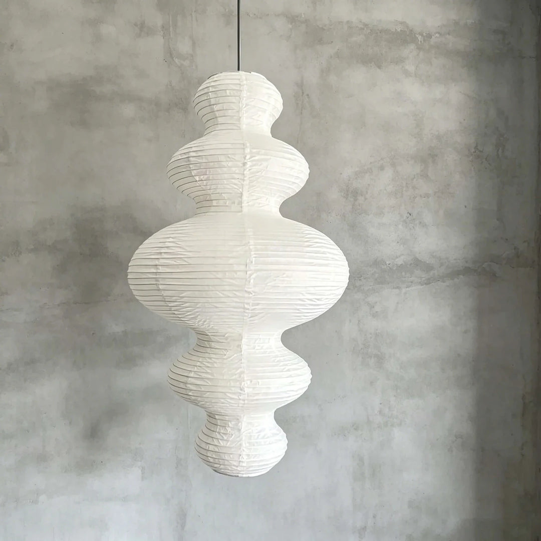 Sculptural paper pendant hung against a textured grey concrete wall