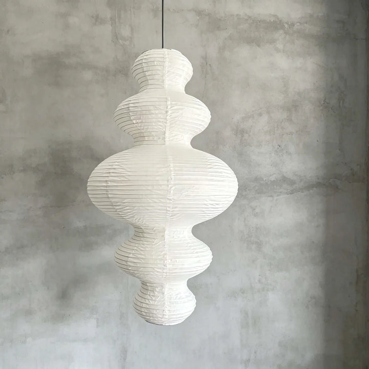 Sculptural paper pendant hung against a textured grey concrete wall