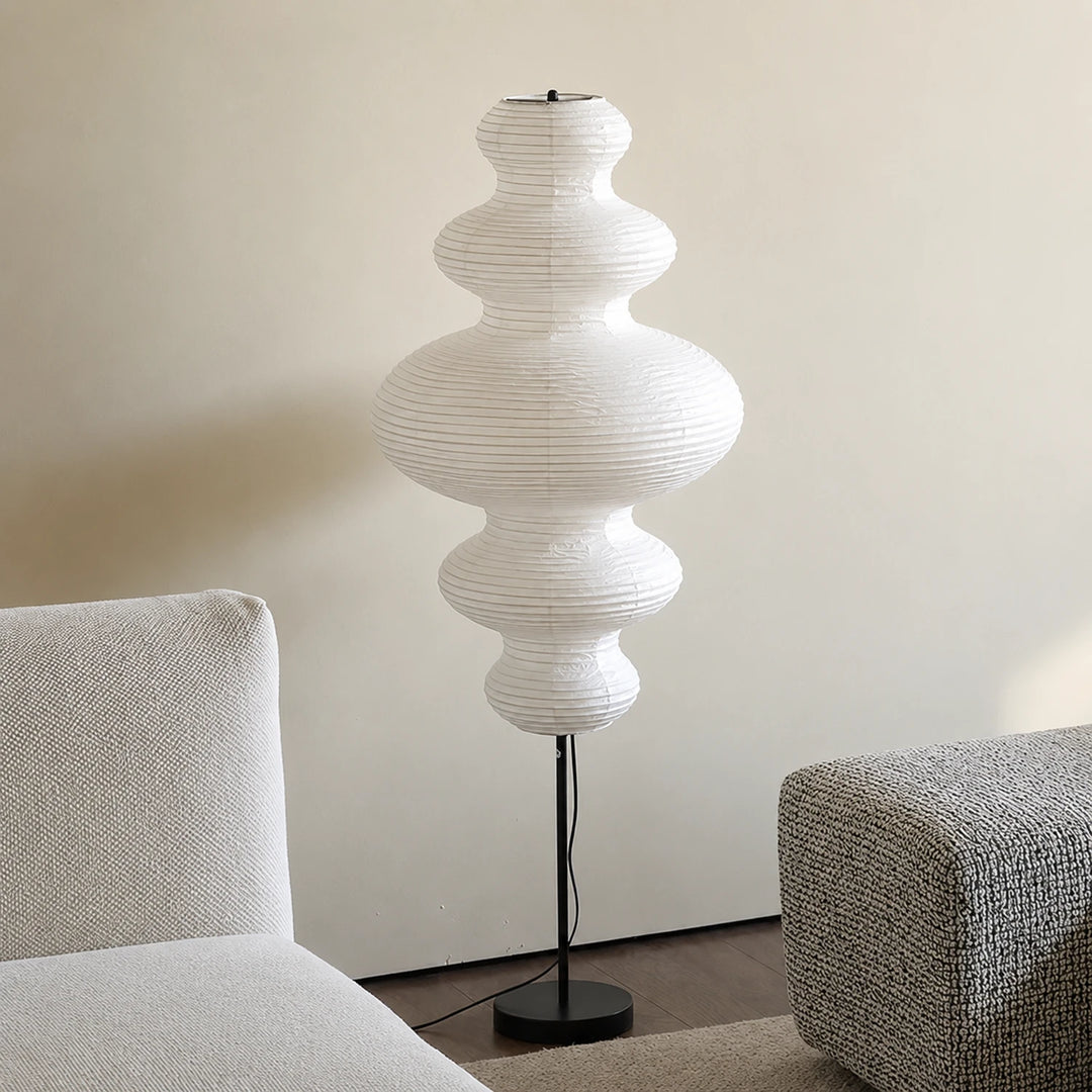 Stacked paper floor lamp in a minimalist corner beside a grey sofa