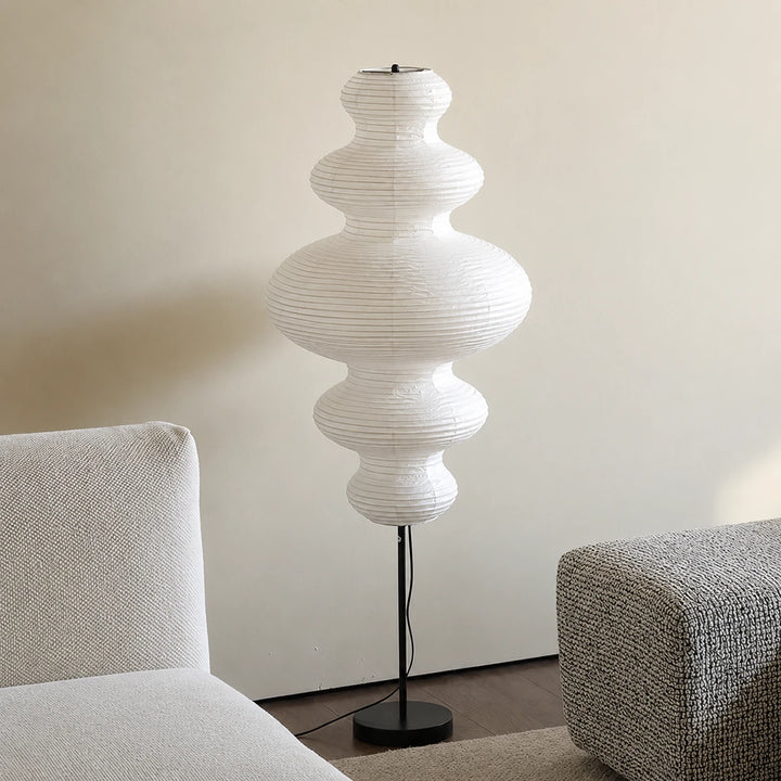 Stacked paper floor lamp in a minimalist corner beside a grey sofa