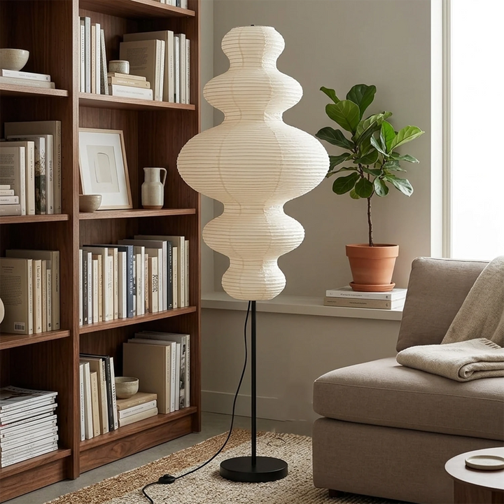 Stacked paper floor lamp glowing in a moody corner beside a bookshelf