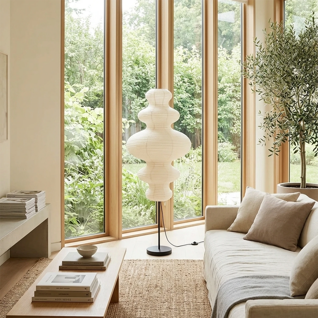 Stacked paper floor lamp by a window with a garden view above a sofa