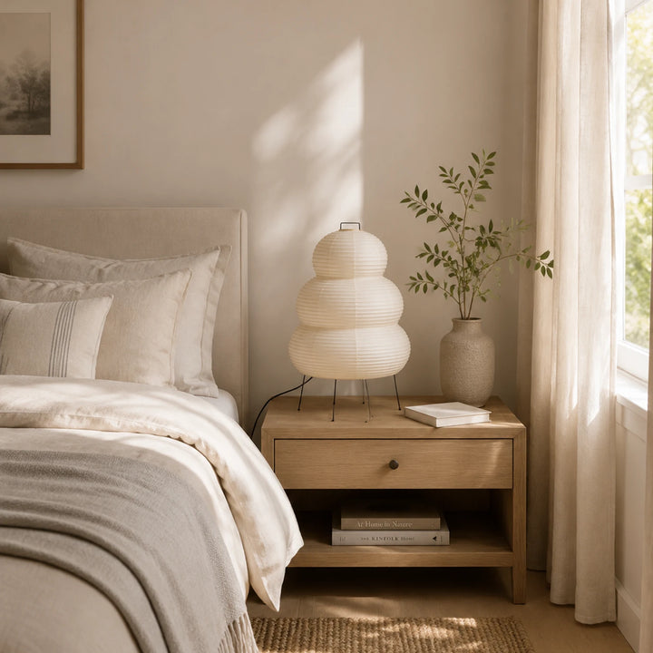 Stacked paper table lamp beside a bouclé armchair in a sunlit window corner