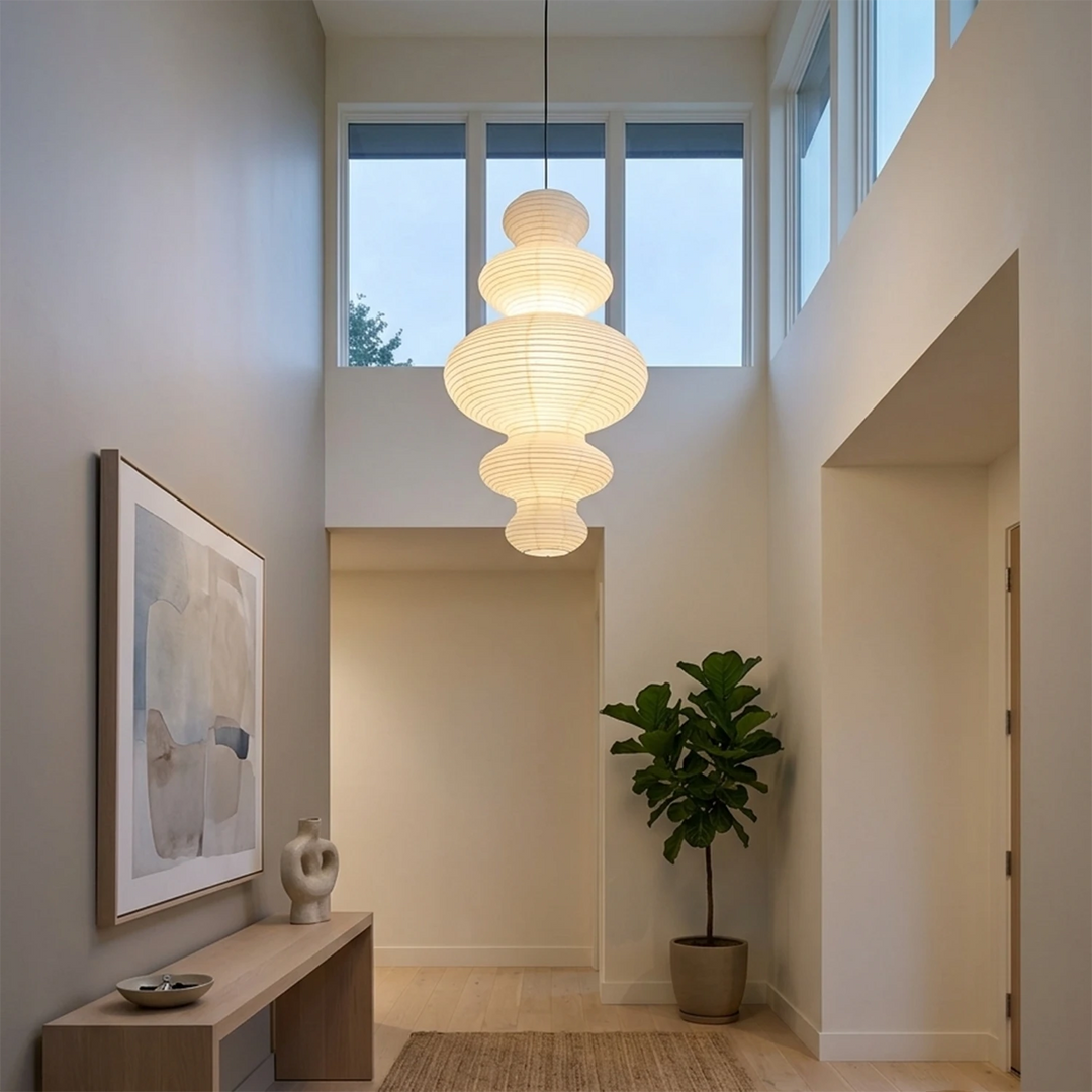 Stacked paper pendant glowing warm in a tall stairwell above a console