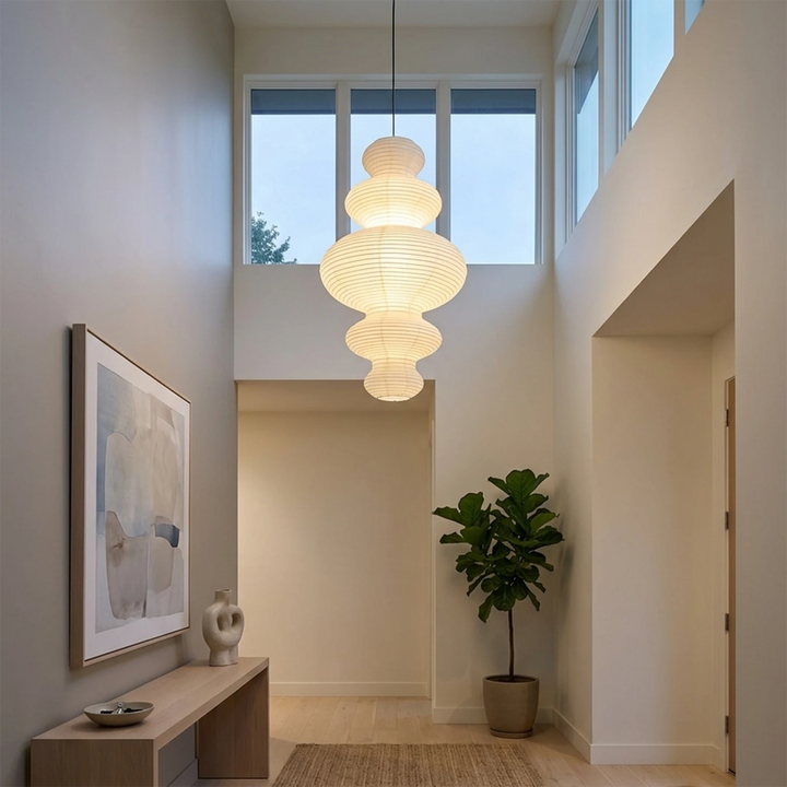 Stacked paper pendant glowing warm in a tall stairwell above a console