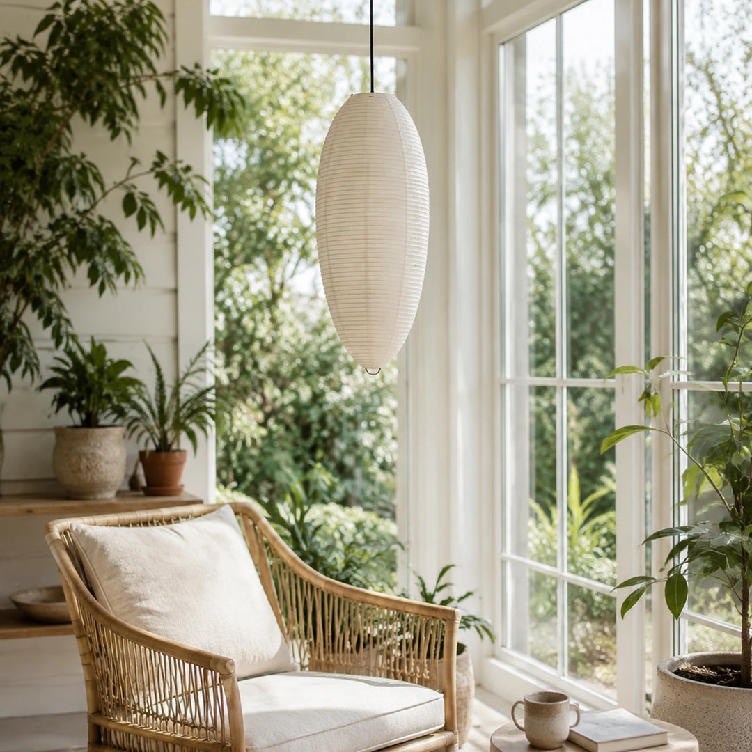Oval paper pendant glowing in a plant-filled sunroom beside a rattan chair