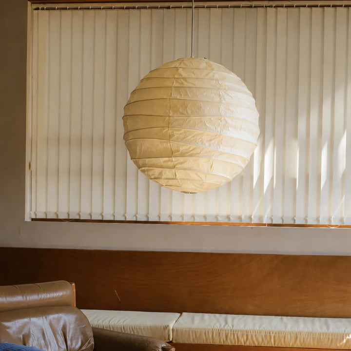 Paper pendant glowing softly in front of sheer floor-length curtains