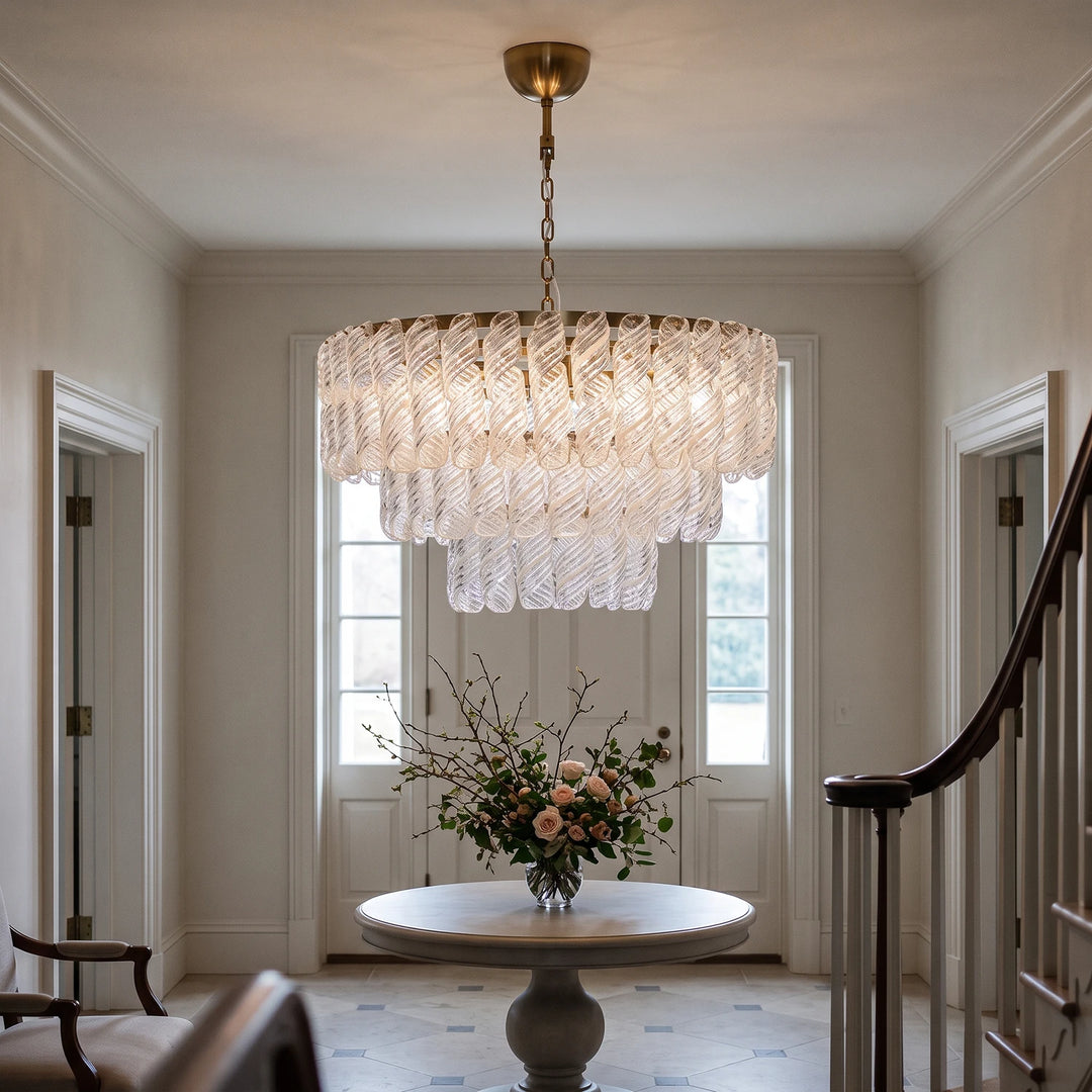 Three tier glass chandelier above a round foyer table with a full floral arrangement beside a staircase