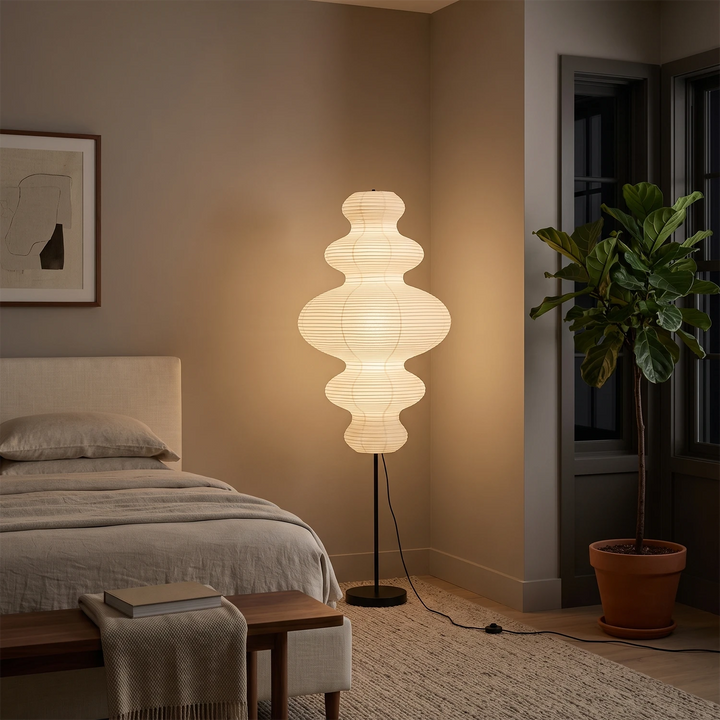 Tiered gourd paper floor lamp glowing beside a bed in a warm bedroom