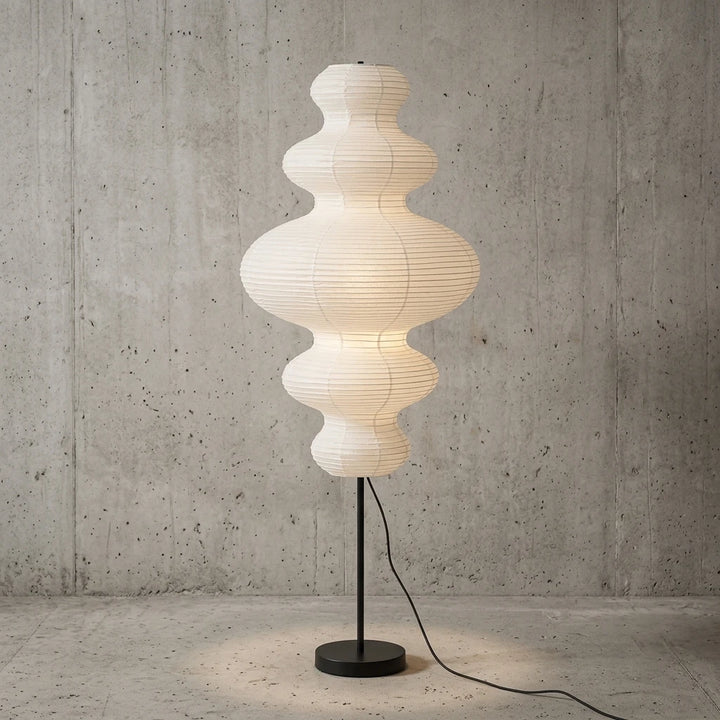 Tiered gourd paper floor lamp lit against a grey concrete studio wall