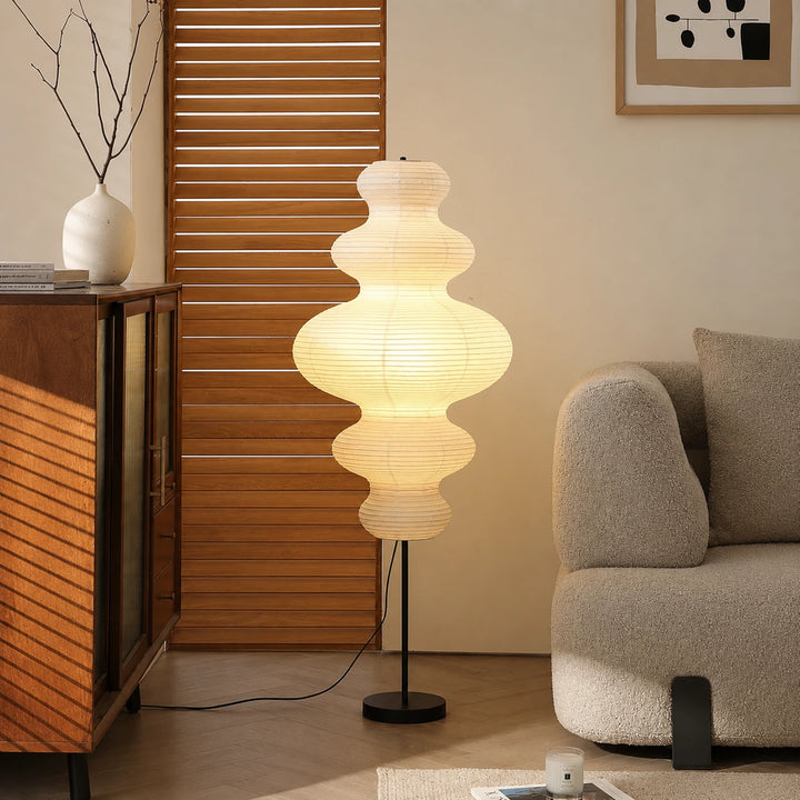 Tiered gourd paper floor lamp glowing warm beside a wooden slat screen
