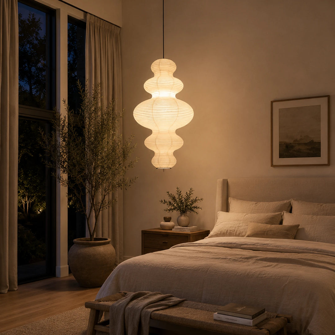 Tiered gourd paper pendant glowing beside a bed in a warm bedroom