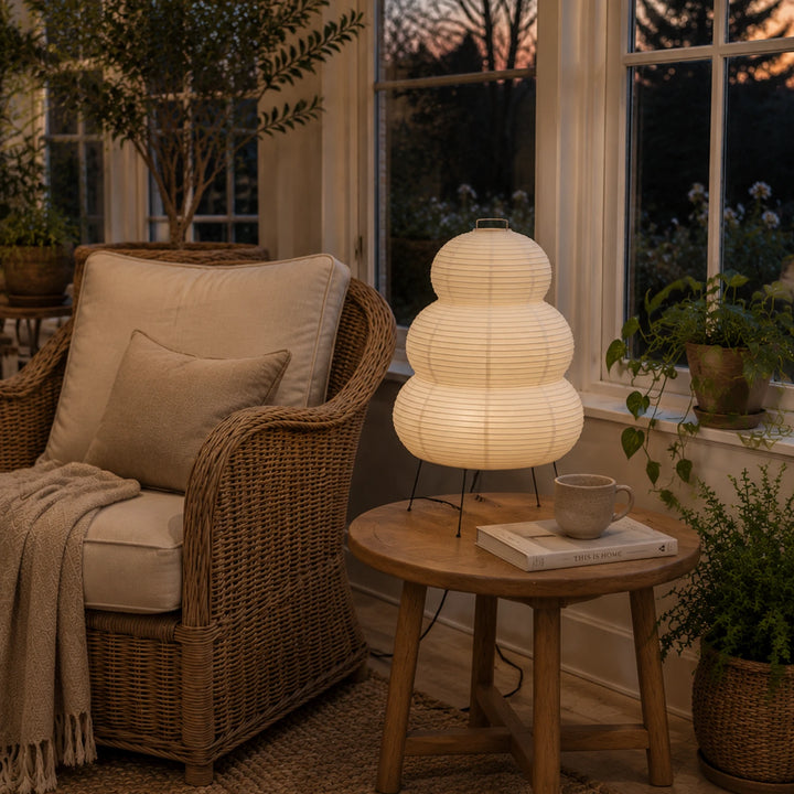 Tiered paper lamp on a round side table beside a rattan armchair